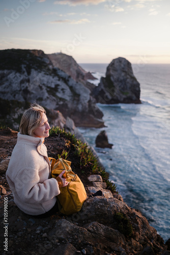 A woman looks out over the Atlantic Ocean while sitting on the rocks, Sintra, Portugal. photo