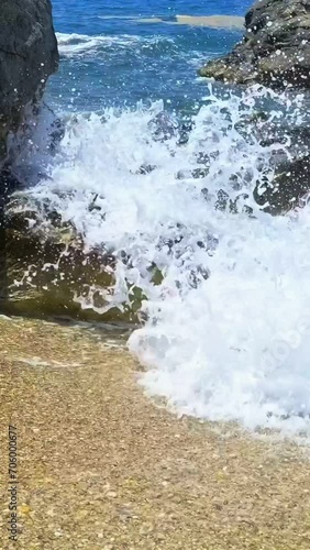 Clear blue sea waves splash and spray on dark polished stones and yellow pebbles on beach, sunny summer day, Greece photo
