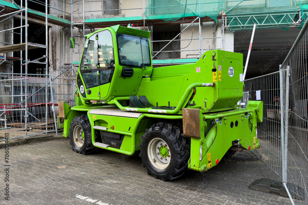 Small green construction machine against the background of a building under construction in scaffolding.