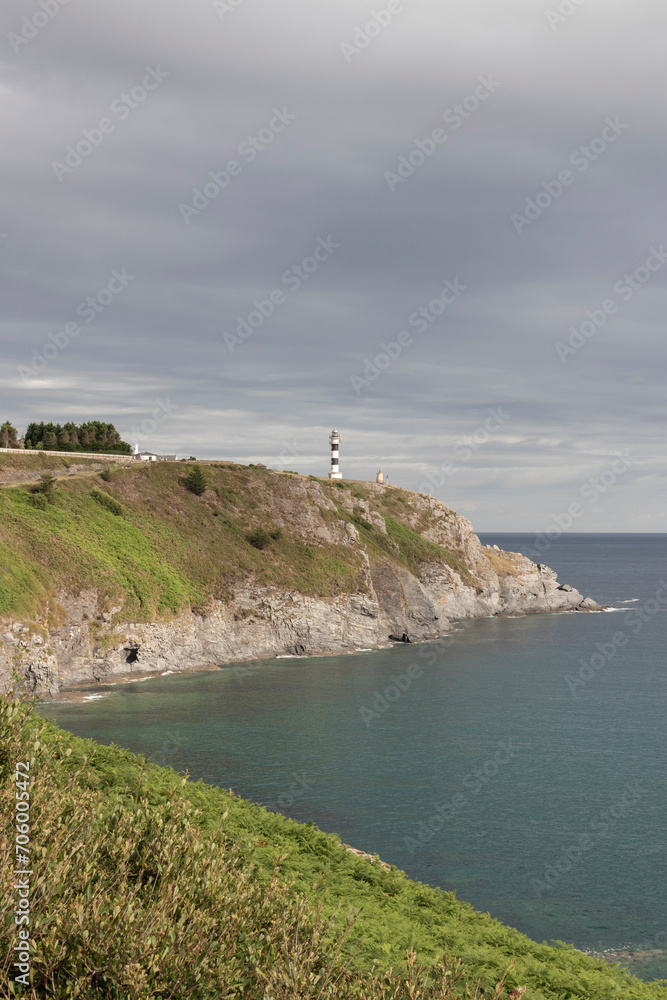 A scenic view of a lighthouse on a cliff, overlooking a calm sea under a partly cloudy sky