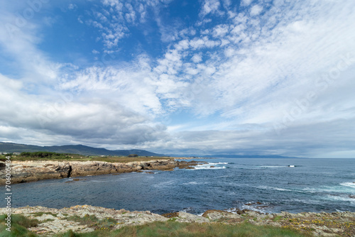 A scenic coastal landscape with rocky shores, blue ocean waves, and a sky filled with fluffy white clouds