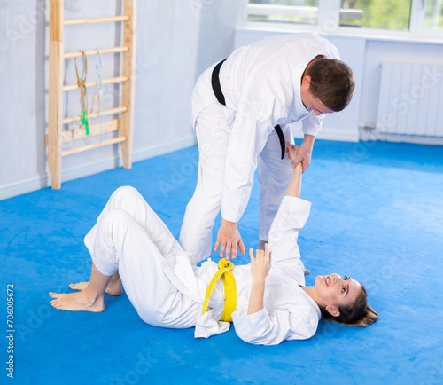 Coach teaches a young woman techniques for wrestling and throwing on sports mats during judo training