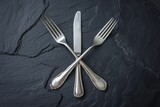 Silver fork and knife crossed on a black slate background