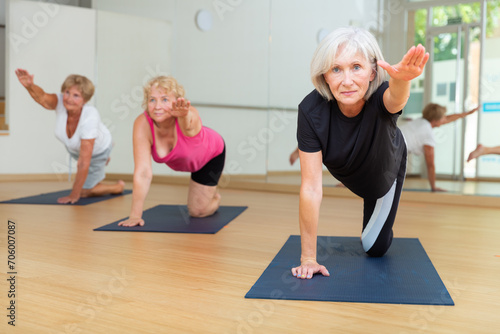 Mature active women who attend group classes in a fitness studio perform a stretching exercise