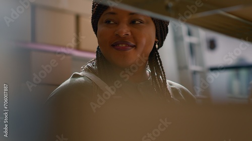 Cheerful african american warehouse quality assurance manager holding tablet, checking packaged products in cardboard boxes, ensuring errorless operations in professional storage hub photo