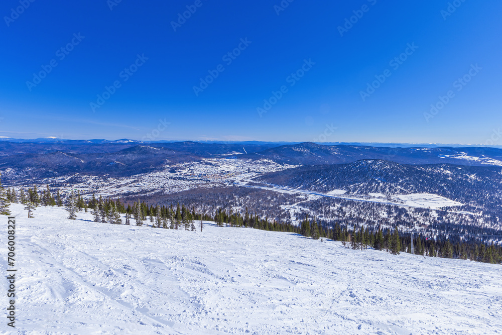 View from mount Green of Sheregesh village, snow ski slopes, beautiful panorama with range mountains and hills far away, fir trees forest, blue sky, picturesque winter nature, sunny weather.