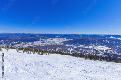 View from mount Green of Sheregesh village, snow ski slopes, beautiful panorama with range mountains and hills far away, fir trees forest, blue sky, picturesque winter nature, sunny weather.