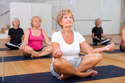 Aged woman who cares about her health and does yoga in a group workout, sits in a half-lotus position in a fitness studio