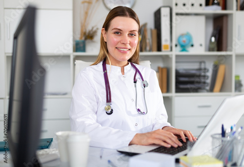 Female doctor in medical uniform is working with documents and laptop