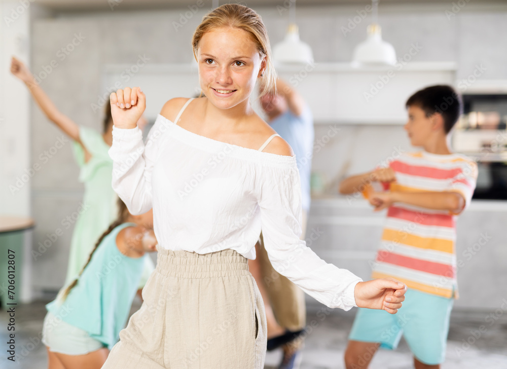Fototapeta premium Behind cheerful positive girl, big family of parents, sisters, brother is rejoicing, dancing, having fun. Family with school-age children celebrates important event date