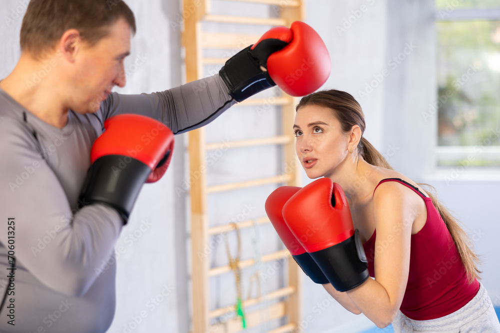 Woman and man in sportswear are engaged in boxing sparring in the gym