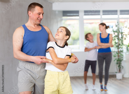 Happy father and preteen daughter practicing dance in pairs together with other family members during training session