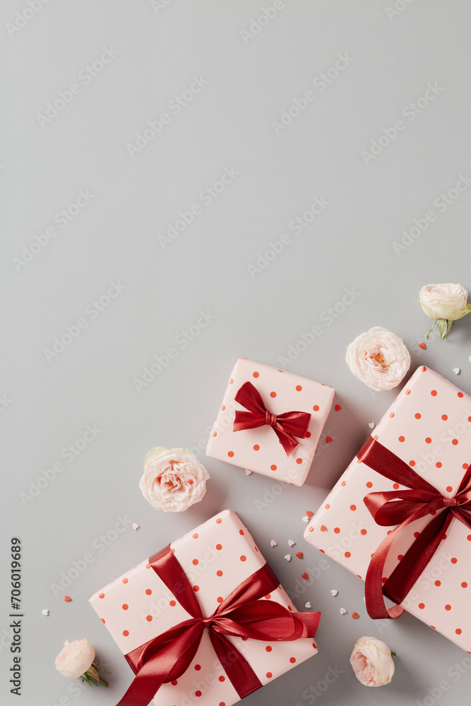 Pink gifts decorated hearts and red ribbon bow, roses buds, confetti on grey background. Happy Valentines Day vertical background.