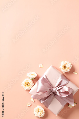 Gift box with pink ribbon bow  rose buds on peach color background. Happy Valentines vertical banner design
