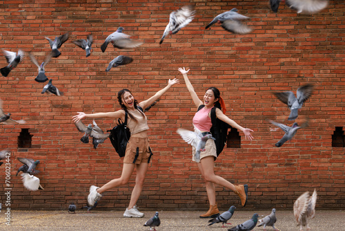 two asian tourist girl happy standing posing and pointing hand while the pigons fly and eat at the tha phae gate, chiang mai thailand,