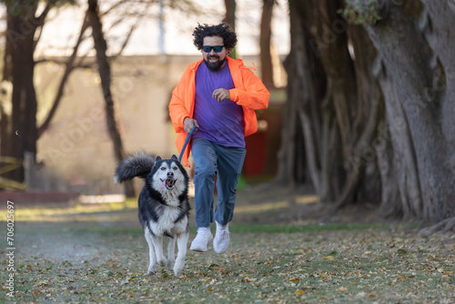 Young Latino man with sunglasses, hair and beard running with his husky dog in park