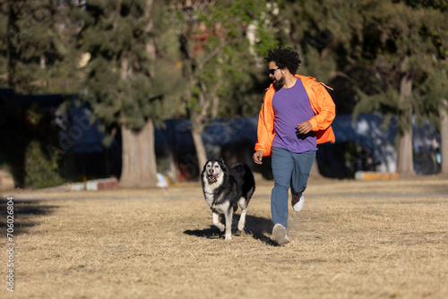 Mexican man with curly hair, beard and sunglasses running in a park with his husky dog