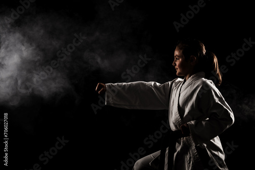 Young girl exercising karate. Child in kimono with smoke in the background.