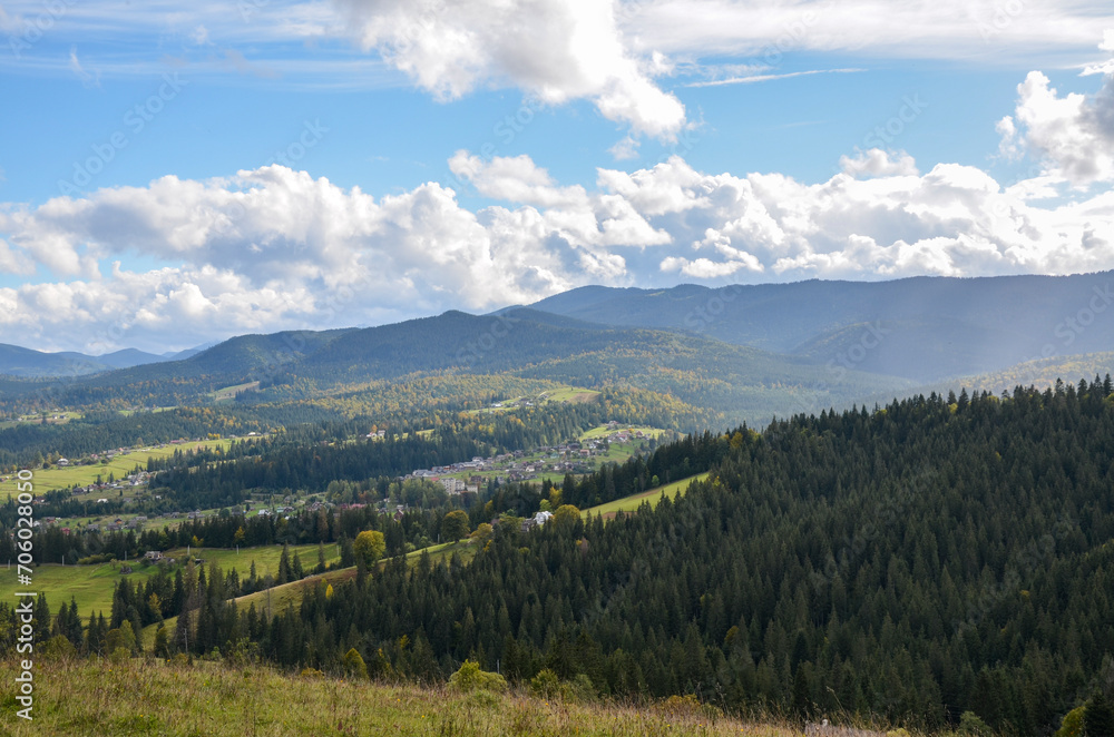 Scenic view of Carpathian village with small houses on the hills surrounded Green spruce forests and mountains on the background