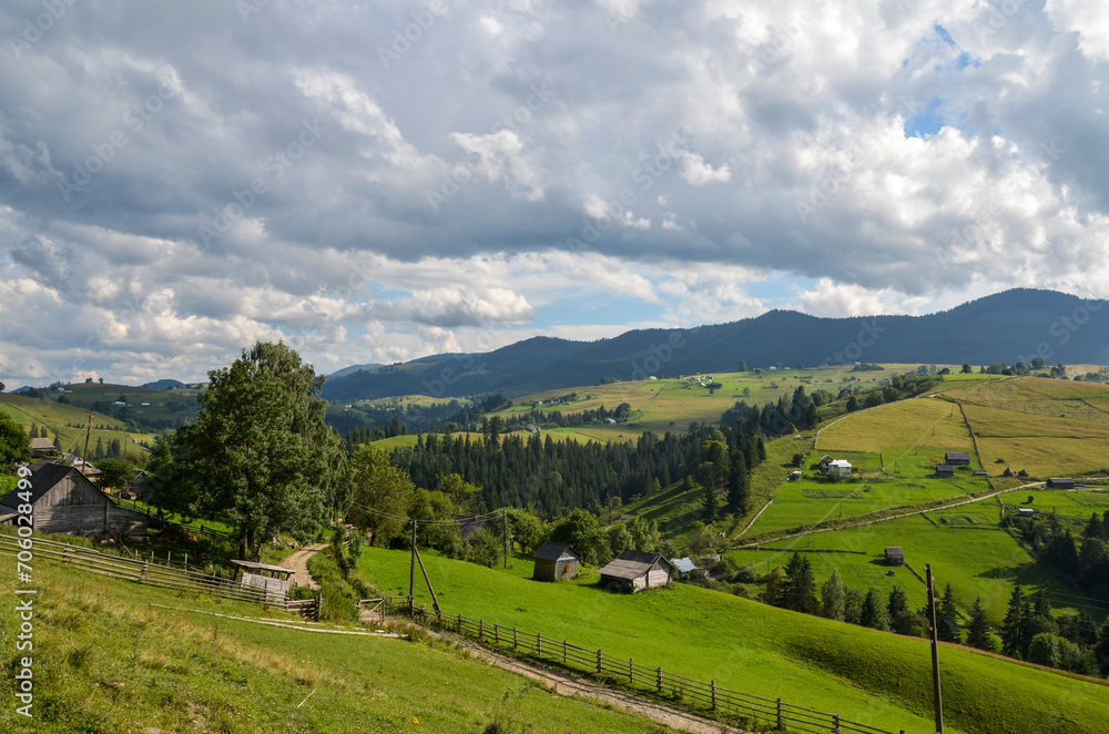 Beautiful landscape with mountain valley, small village on the hills, lush meadows covered green grass and trees. Carpathian Mountains in summer