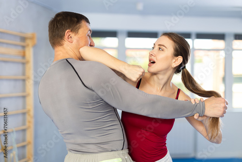 Adult man and young woman practice self-defense techniques at gym..