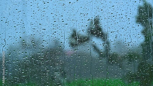 Rainy weather with trees swaying in the strong wind visible through wet window glass