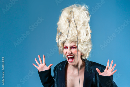Weird yelling princess, queen wearing black jacket, and vintage royal wig with red makeup scream isolated on blue background. Concept of comparison of eras, modernity and renaissance, beauty photo