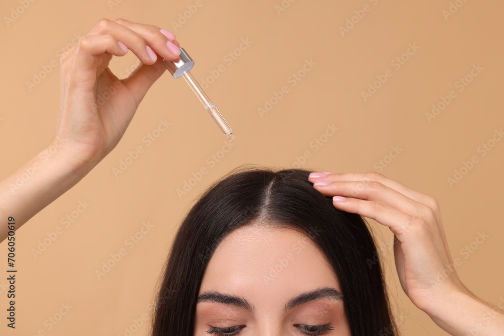 Obraz premium Woman applying hair serum on beige background, closeup. Cosmetic product