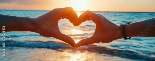 Two couple hands making heart symbol on sunset or sunrise beach background, love and compassion concept photo