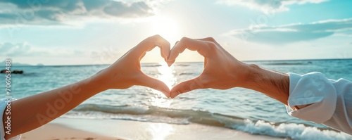 Two couple hands making heart symbol on sunset or sunrise beach background, love and compassion concept photo