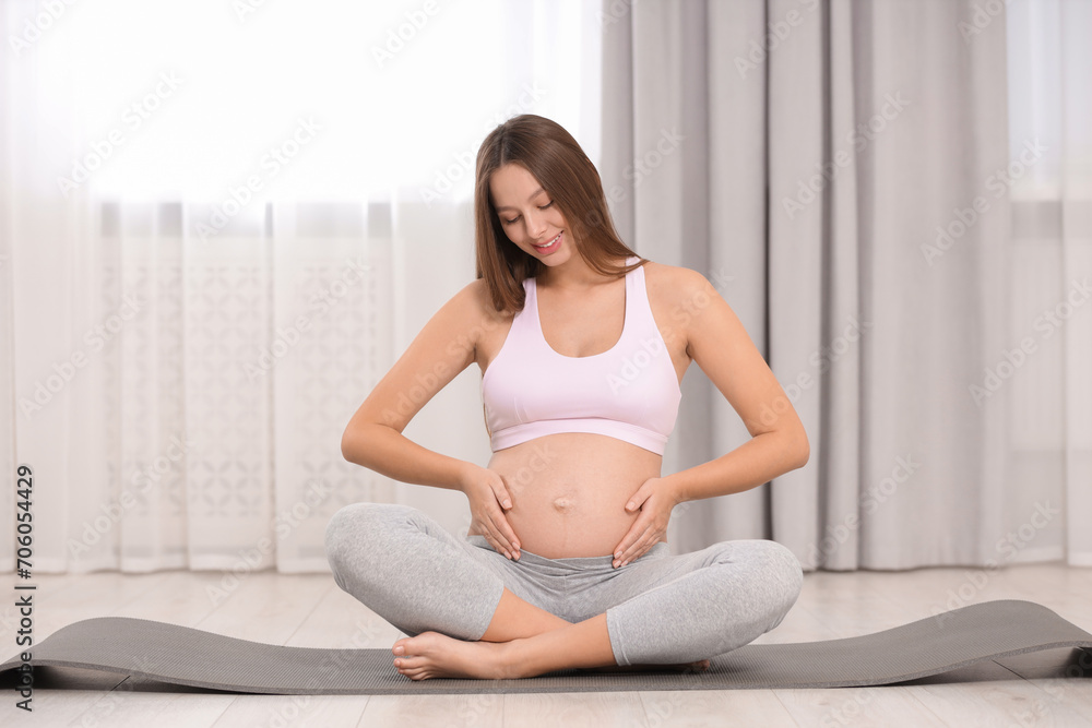 Pregnant woman sitting on yoga mat at home Pregnant woman sitting on yoga mat at home