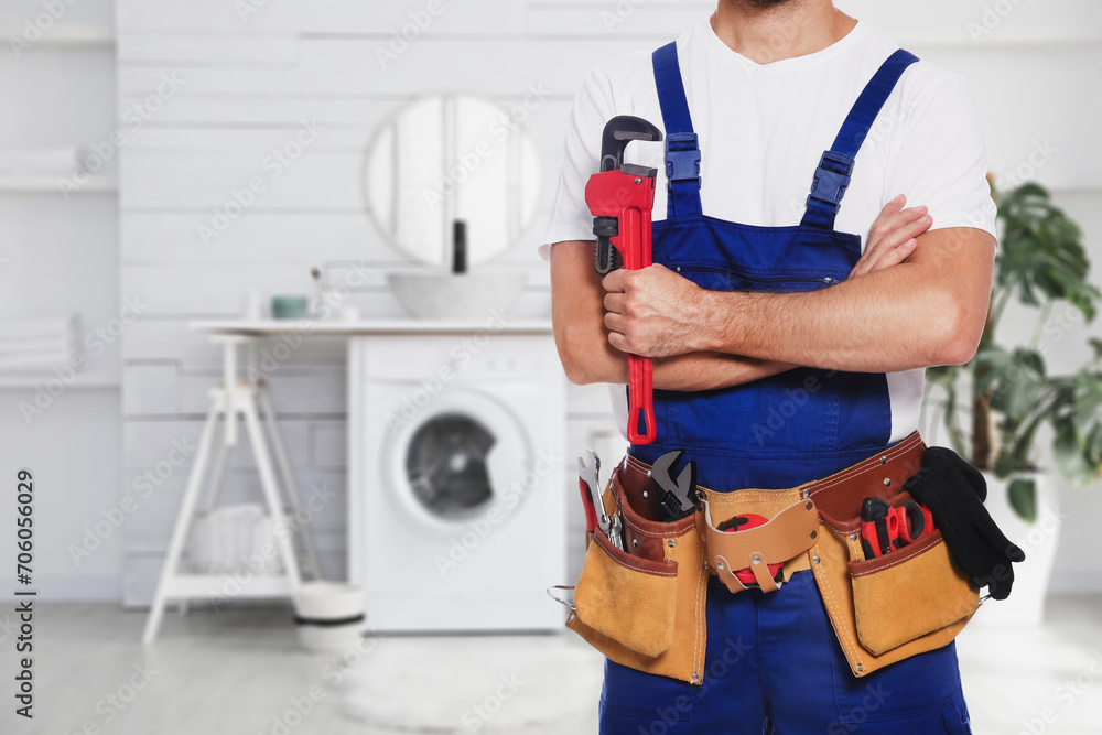 Plumber with pipe wrench and tool belt in bathroom, closeup. Space for text Plumber with pipe wrench and tool belt in bathroom, closeup. Space for text