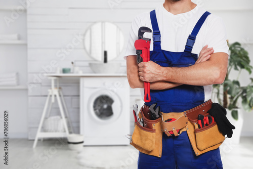 Plumber with pipe wrench and tool belt in bathroom, closeup. Space for text photo
