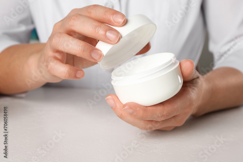 Dermatologist holding jar of cream at white table  closeup. Developing cosmetic product