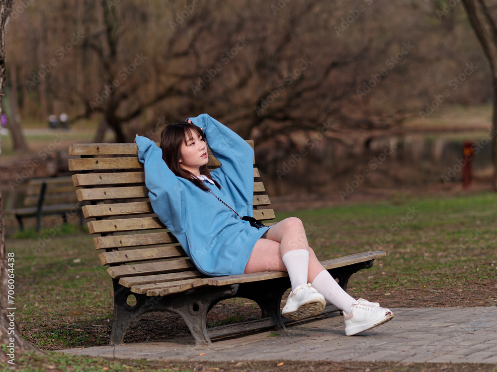 Fototapeta premium Beautiful young Chinese woman posing in sunny summer forest, wearing blue loose oversized top and miniskirt with small shoulder bag. Emotions, people, beauty, youth and lifestyle portrait.