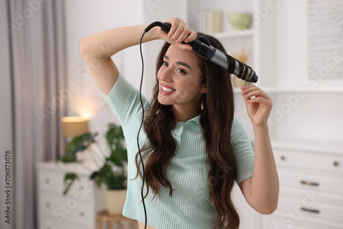 Smiling woman using curling hair iron at home