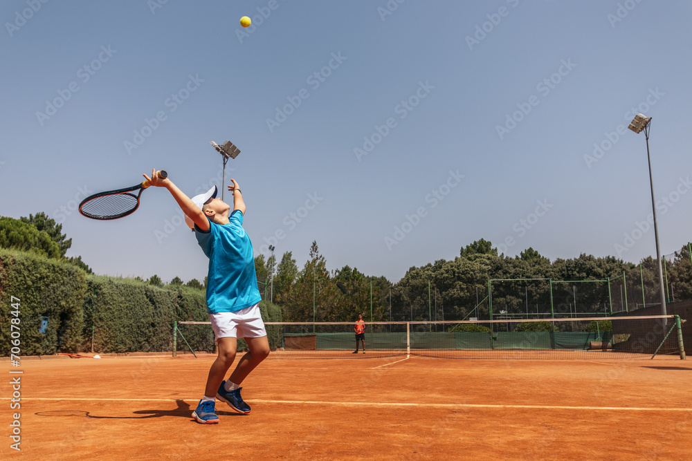 Boy playing tennis with his coach on a dirt court