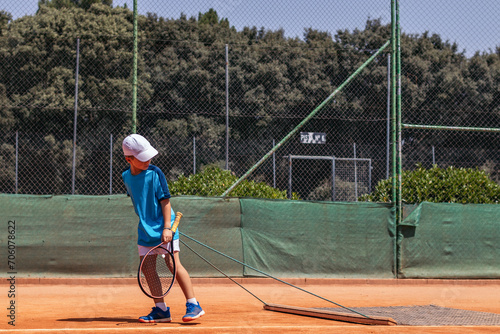 Little boy playing tennis doing court maintenance