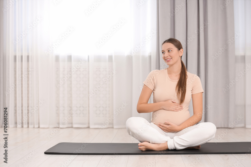 Pregnant woman sitting on yoga mat at home, space for text Pregnant woman sitting on yoga mat at home, space for text