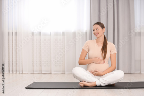 Pregnant woman sitting on yoga mat at home, space for text