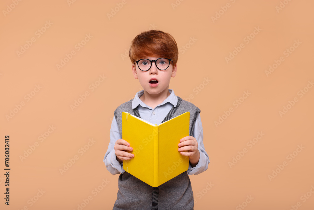 Surprised schoolboy with book on beige background Surprised schoolboy with book on beige background