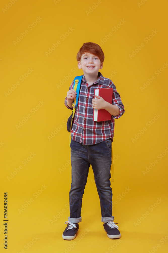 Smiling schoolboy with backpack and book on orange background Smiling schoolboy with backpack and book on orange background