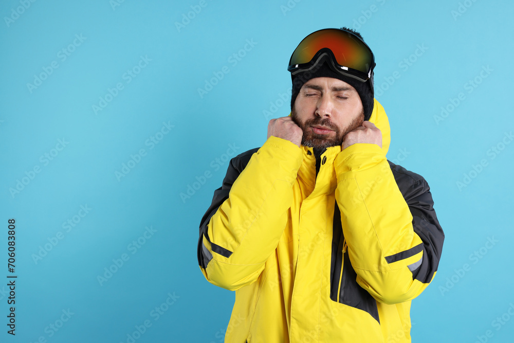 Winter sports. Man in ski suit and goggles on light blue background, space for text
