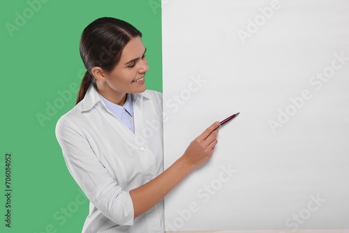 Ophthalmologist pointing at blank banner on green background, space for text photo