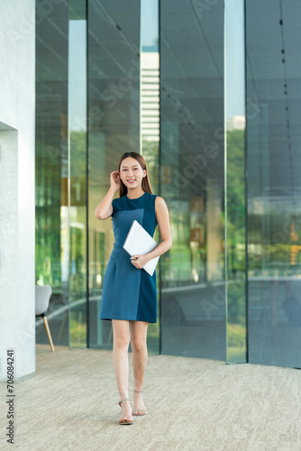 Full Length Portrait of an Asian Business Woman Holding a Laptop with a Elegant Look and Smile