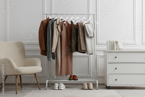 Rack with different stylish women`s clothes, shoes, dresser and armchair near white wall in room © New Africa