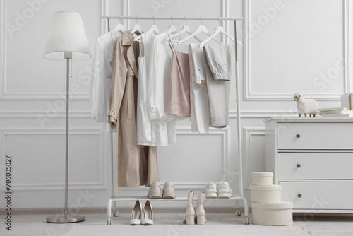 Rack with different stylish women`s clothes, shoes, lamp and dresser near white wall in room photo