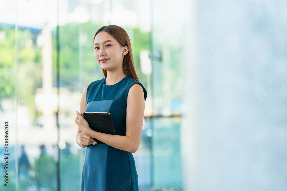 Young Asian Woman Smiles Happily While Using Digital Tablet to Manage Her Tasks Remotely While Out Of Office Young Asian Woman Smiles Happily While Using Digital Tablet to Manage Her Tasks Remotely While Out Of Office