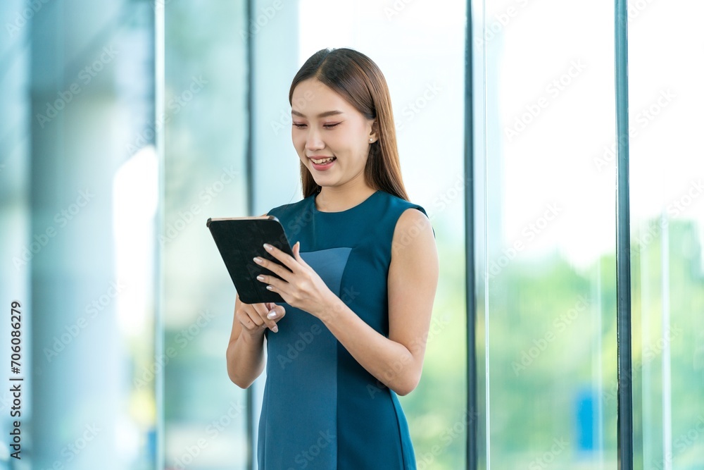 Young Asian Woman Smiles Happily While Using Digital Tablet to Manage Her Tasks Remotely While Out Of Office Young Asian Woman Smiles Happily While Using Digital Tablet to Manage Her Tasks Remotely While Out Of Office