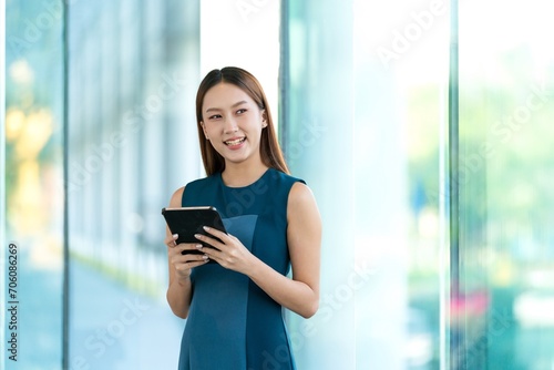 Young Asian Woman Smiles Happily While Using Digital Tablet to Manage Her Tasks Remotely While Out Of Office